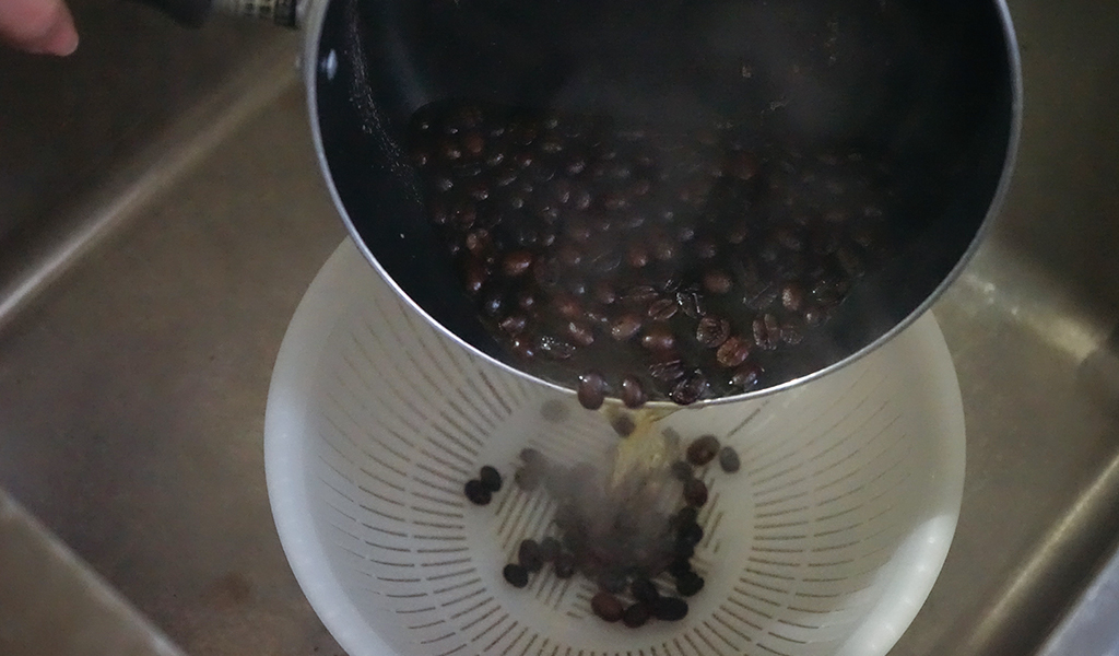 茹でたコーヒー豆をザルに移す
